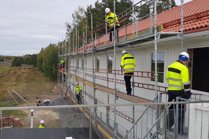 Hotelneubau in Holzbauweise mit Gerüst, drei Monteure in Warnkleidung auf der Gerüstlage