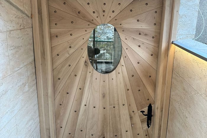 Eingebaute Haustür nach Maß mit strahlenförmig verlegtem Holz, ovalem Fenster und geschmiedetem Griff