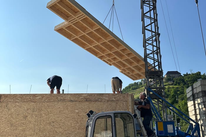 Vorgefertigtes Wandelement aus Holz hängt am Kran über einer Baustelle