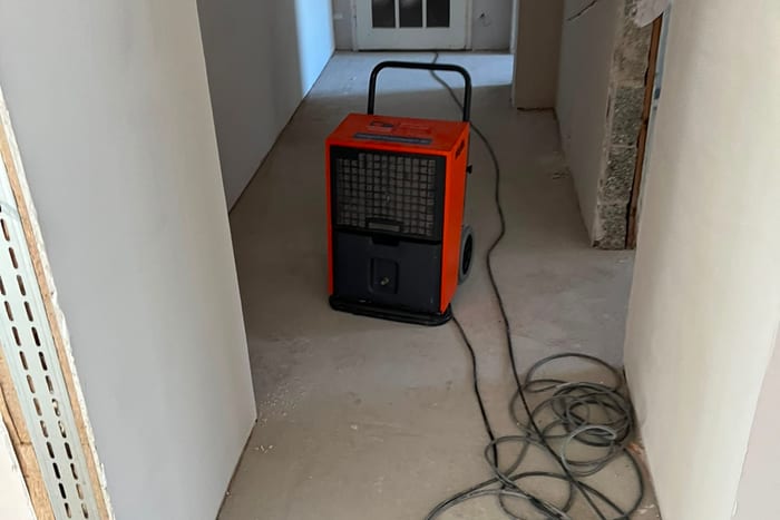 Bautrockner im Flur einer Wohnung nach einem Wasserschaden, Schlauch und Kabel auf dem freigelegten Estrich