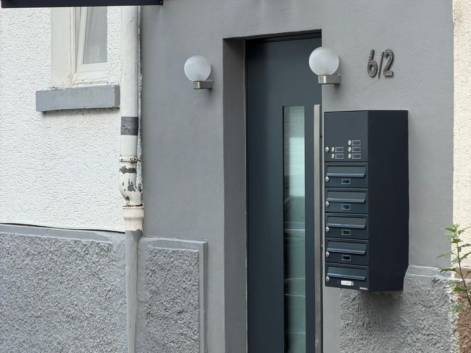 Sanierter Hauseingang mit neuer anthrazitfarbener Tür, Vordach und Briefkastenanlage